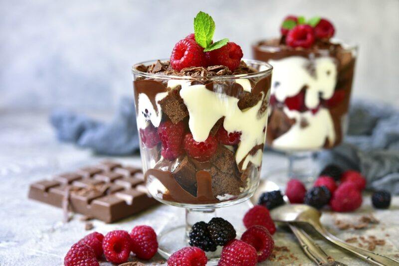 Two glasses of a layered raspberry brownie cheesecake trifle on a table