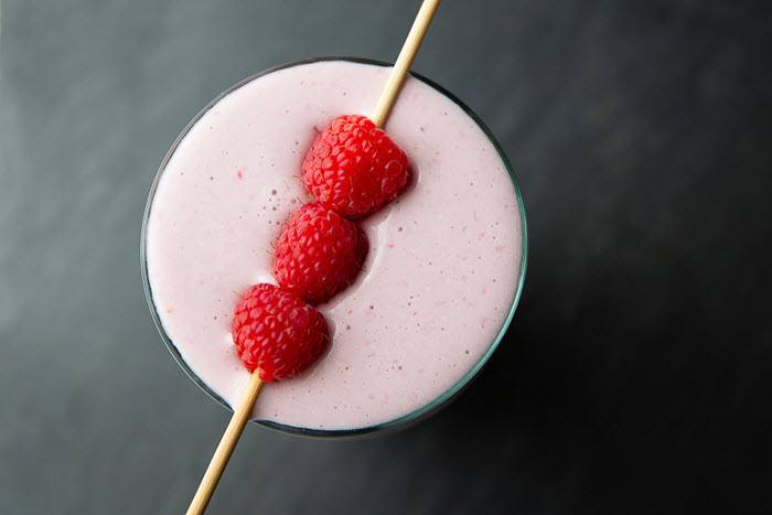 A raspberry smoothie with three suspended raspberries on a black background