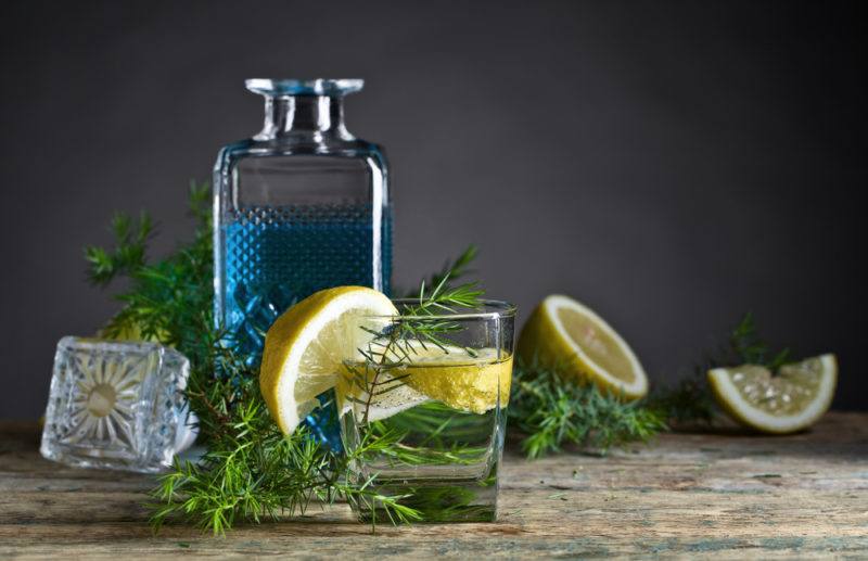 A bottle of blue gin with various garnishes, lemon wedges and glasses of gin and tonic