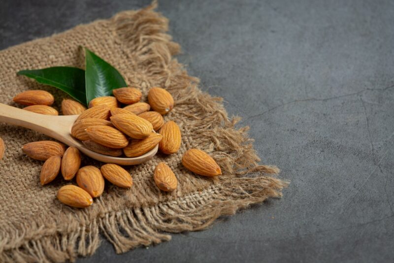 A piece of brown cloth or burlap with raw almonds on it, along with a wooden spoon of more almonds