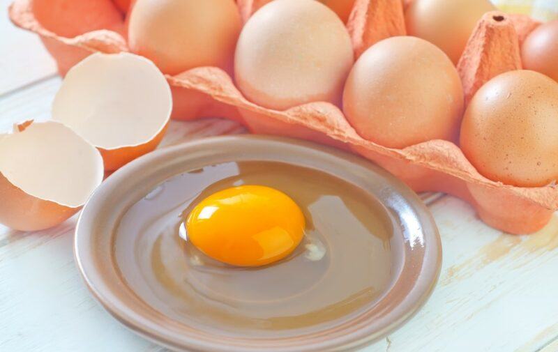 A small flat plate with a single egg, next to egg shells and a container of whole eggs