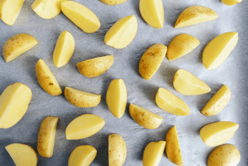 A baking tray with a collection of raw potatoes that have been cut into wedges