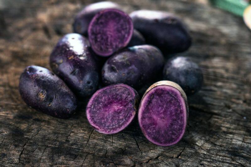 A collection of raw purple potatoes outside, one of which has been sliced in half