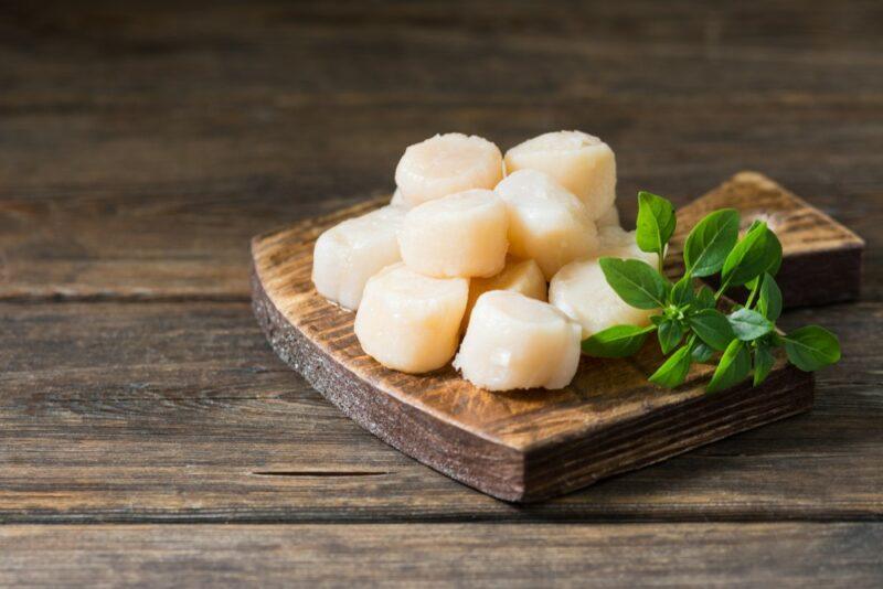 A small wooden dish containing raw scallops