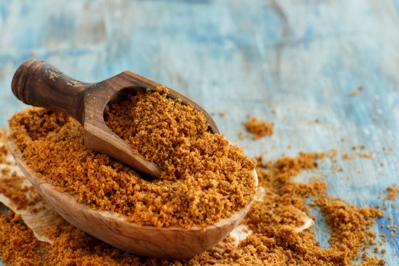 A wooden bowl and scoop that is overflowing with raw sugar