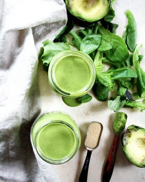 Two green smoothies on a table with avocado and spinach