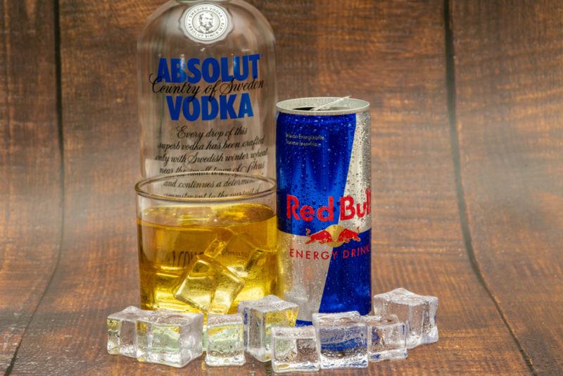 A bottle of Absolut Vodka, a can of Red Bull and a glass containing the two mixed with ice