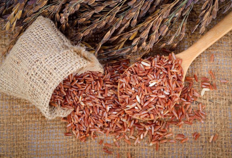 Red rice spilling out of a burlap bag and more red rice on a wooden spoon