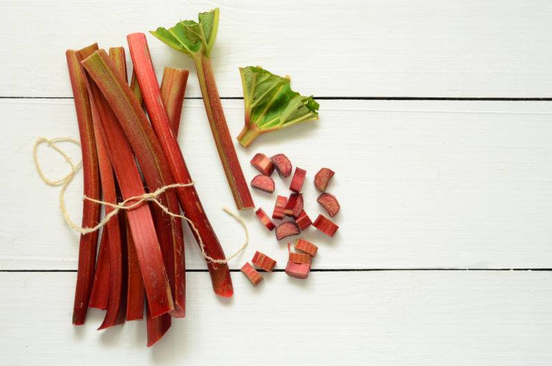 Rhubarb stems in a bundle on a table, with one of the stems cut up