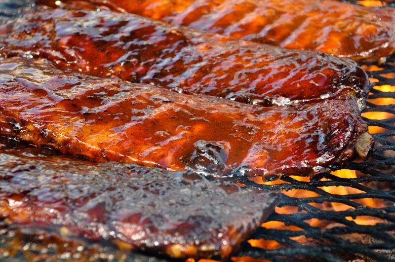 4 Racks of Ribs with Sauce sitting on a grate over a fire