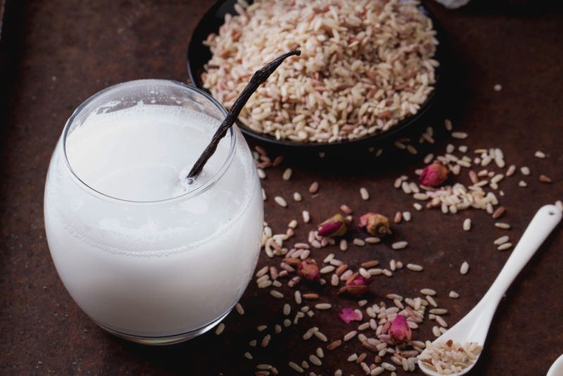 A glass of rice milk next to a bowl of rice and rice scattered on a table