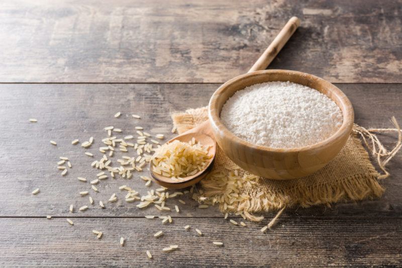 A wooden bowl of rice protein powder, with rice and a spoon