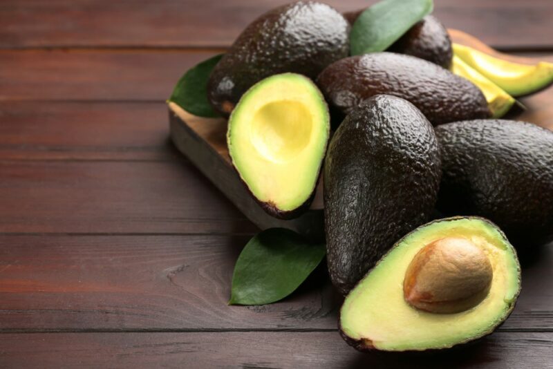 A wooden table with a pile of ripe avocados and one avocado half