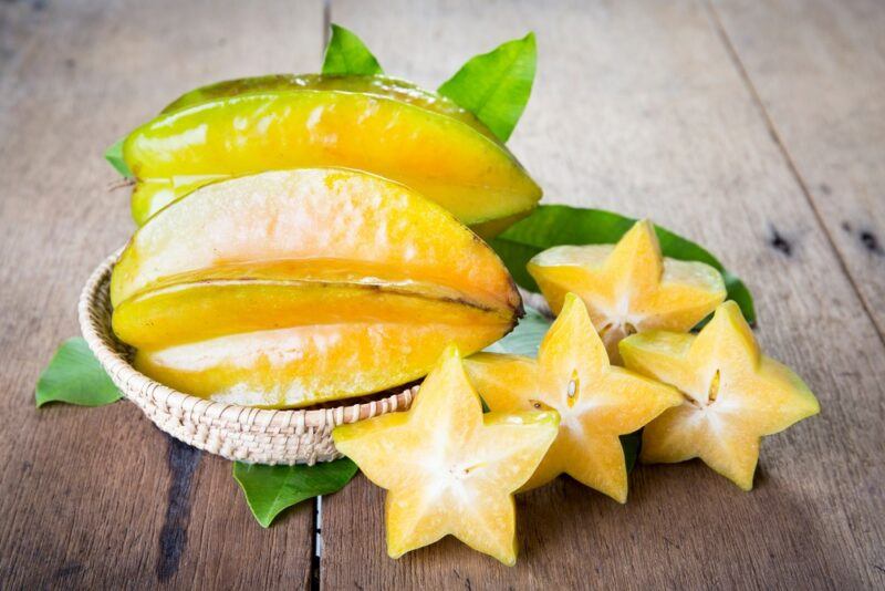 Two large starfruit in a light colored dish, with a few slices of the fruit