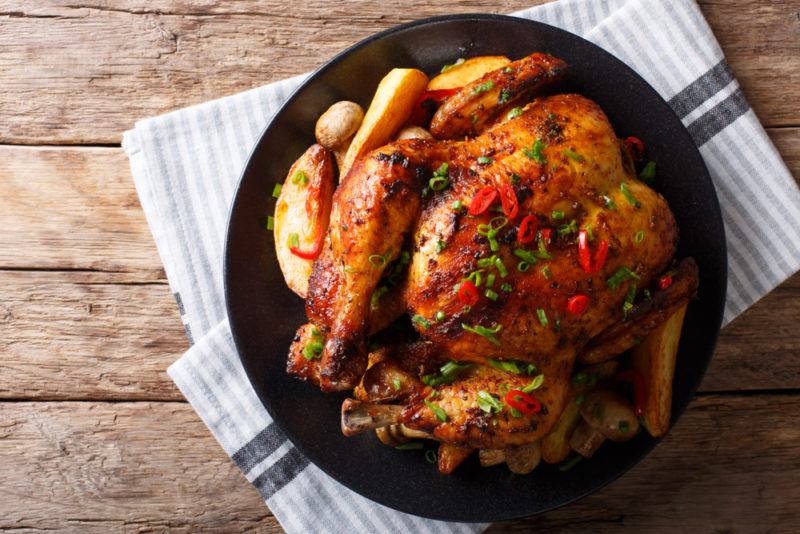 A black plate on a cloth or tea towl that contains a roast chicken, with herbs and cranberries