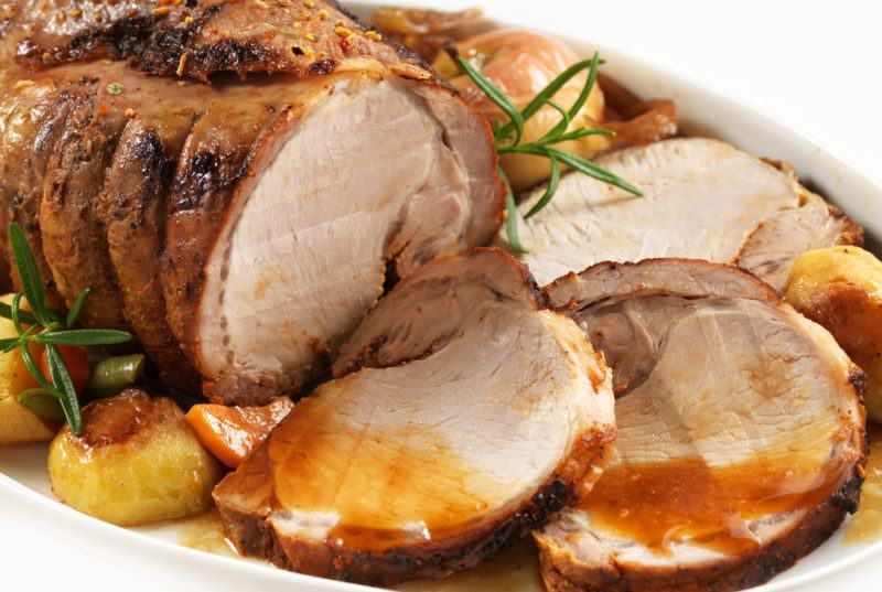 Roast pork with gravy in a white dish, where some of the pork has been sliced