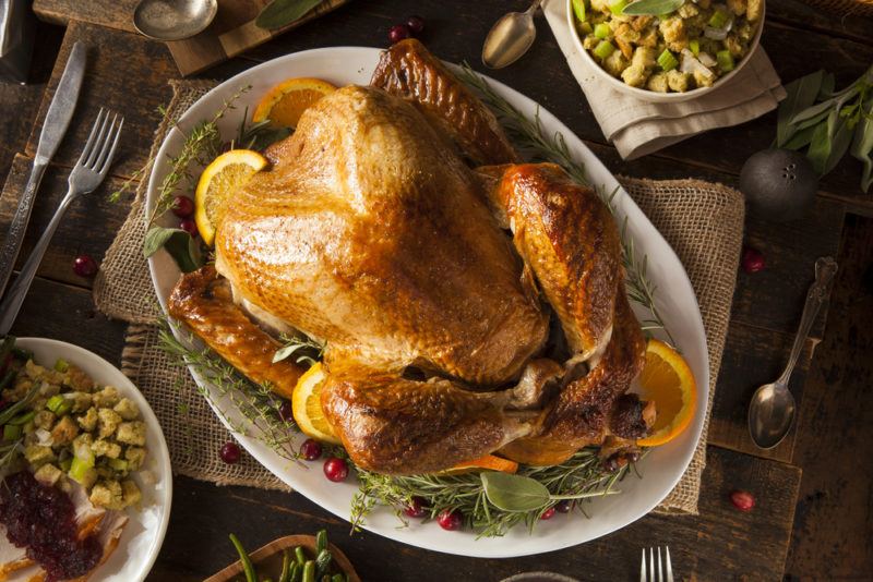 A roast turkey on a white plate, with a few lemons, and sides almost out of the shot