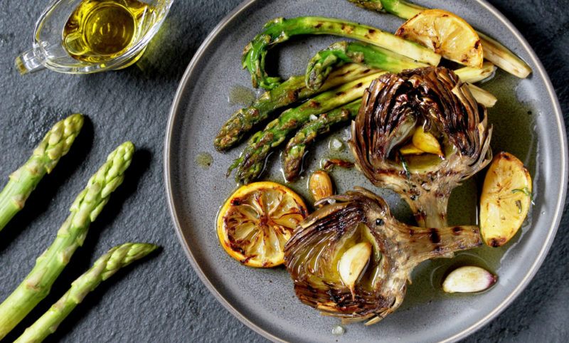 A gray plate that contains roasted asparagus and artichokes