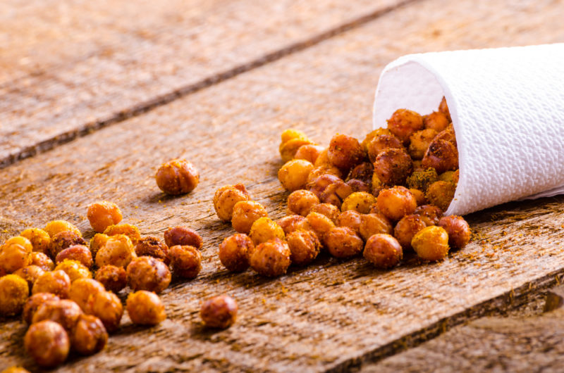 A container of roasted chickpeas spilling out onto a wooden table