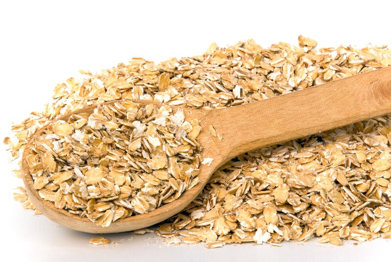 This photo shows a wooden spoon with rolled oats on it and around it against a white background.