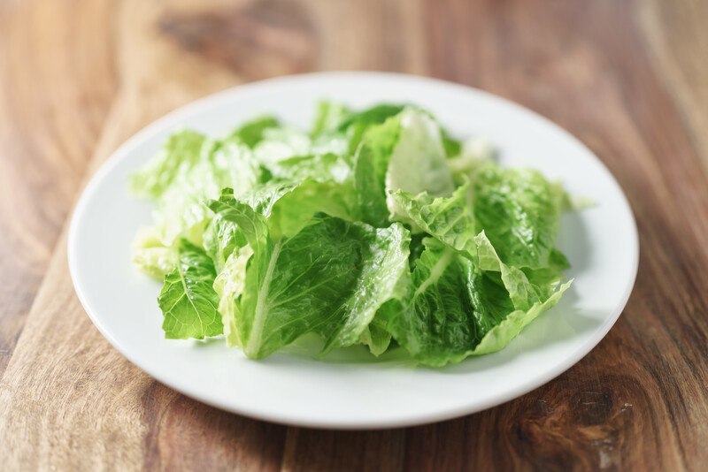 on a wooden surface is a white plate full of fresh Romaine lettuce