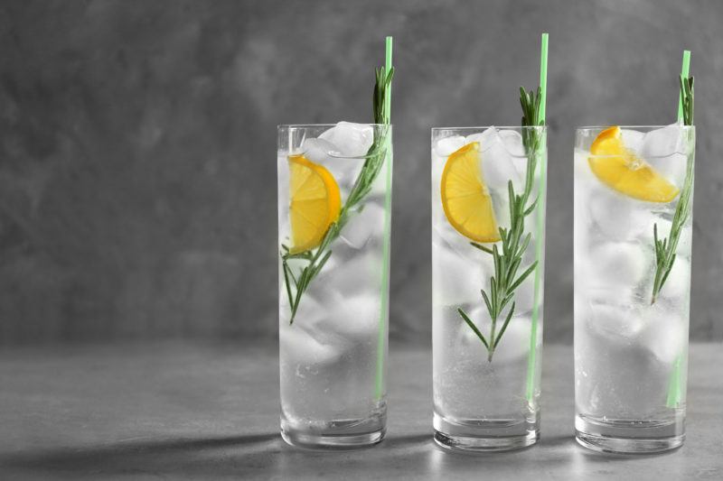 Three tall glasses of gin, rosmary, lemon slices, ice and soada water