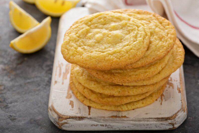 A wooden board with a stack of rosemary, lemon, and white chocolate cookies