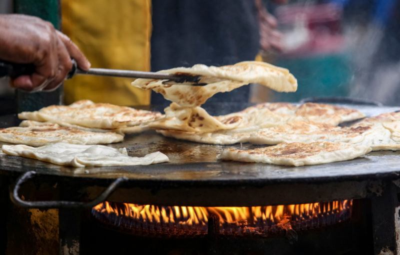 A street vendor with a grill preparing rotis