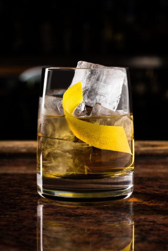 A rusty nail cocktail with ice and a lemon peel