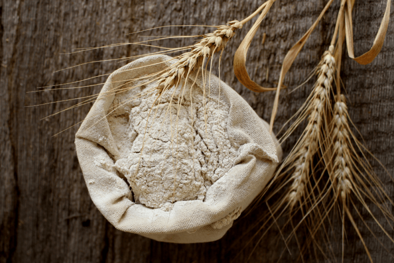 A wooden table with a sack of rye flour, plus some rye stalks