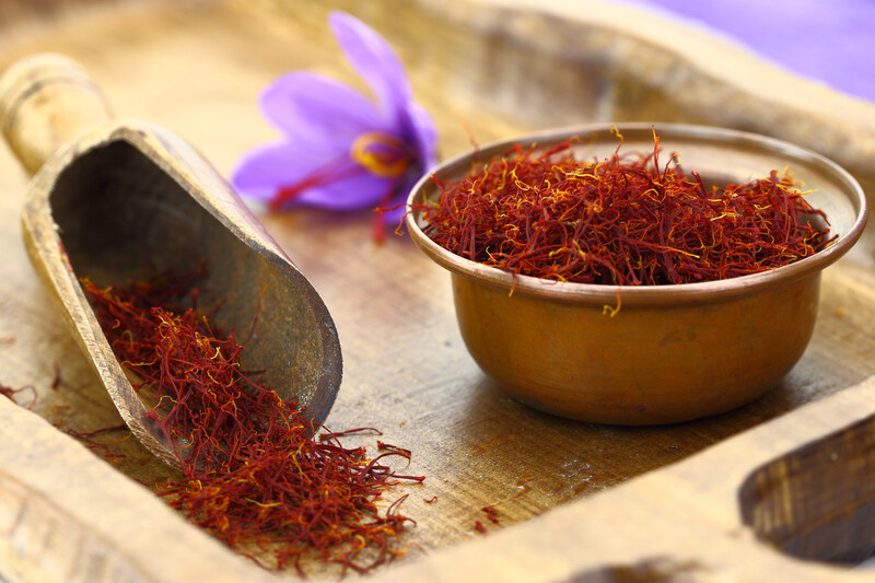 Wooden scoop and small copper bowl with saffron, on a wooden tray with one single saffron flower at the back.