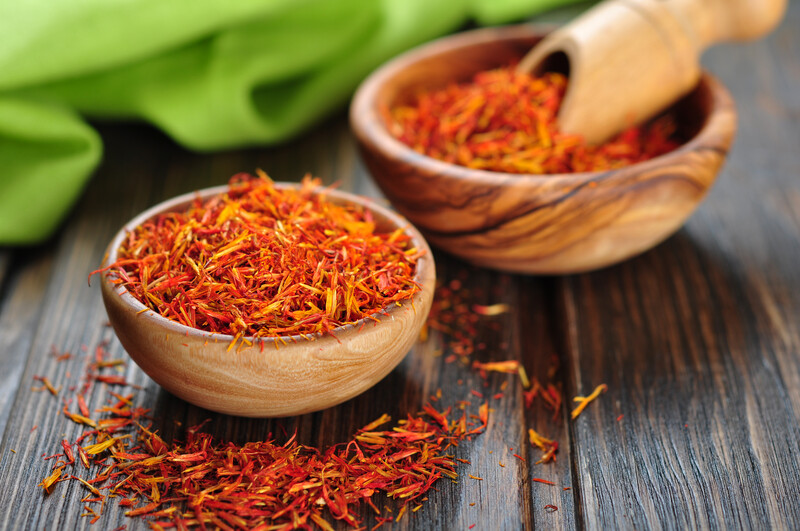 two small wooden bowls full of saffron, resting on a wooden table with loose saffron bits around it.