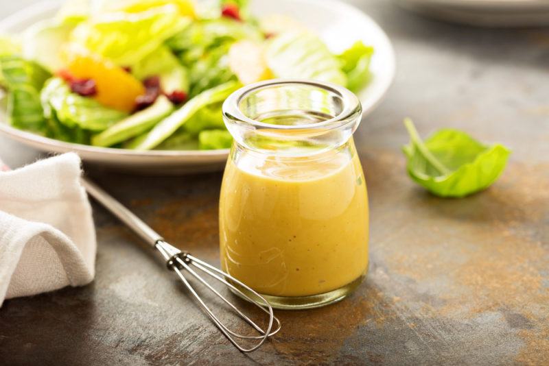 A white bowl containing salad, with a glass container of salad dressing