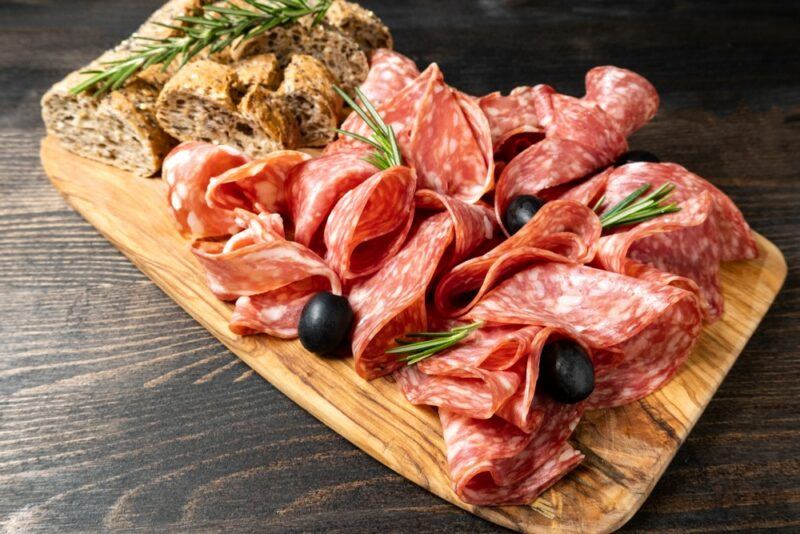 A wooden board with salami, olives, and bread