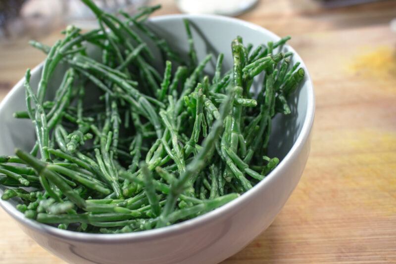 on a wooden surface is a white bowl with salicornia