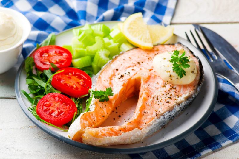 A freshyly cooked salmon dinner, which includes a small salad and lemon wedges