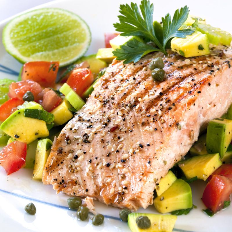 Salmon steak served with sliced zucchinis and red bell peppers served with lime