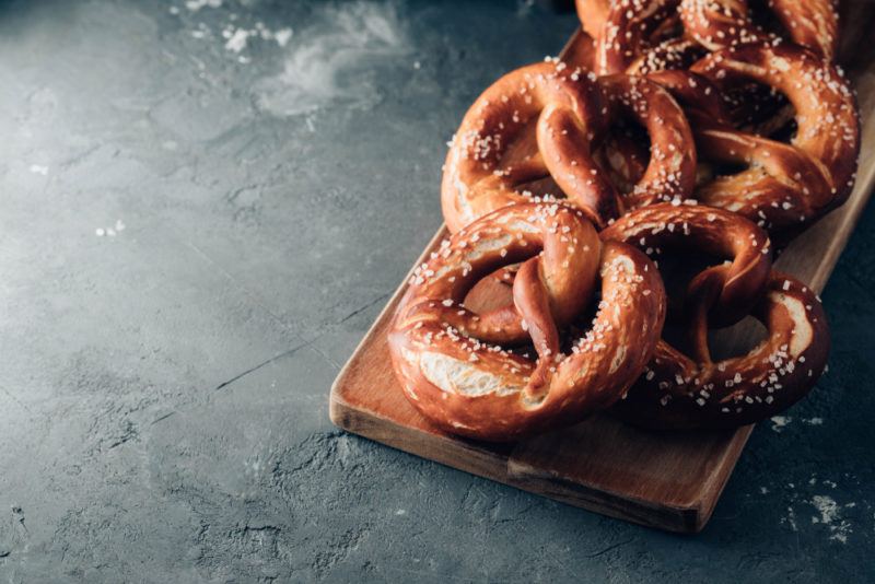 Fresh pretzels with salt on a wooden board that's on a gray table