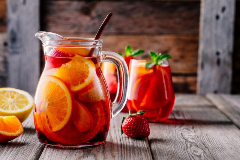 A pitcher with a sangria cocktail and a glass of the cocktail in the background