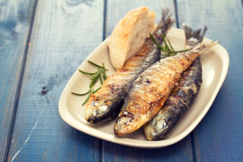 A white plate with cooked sardines on a blue table