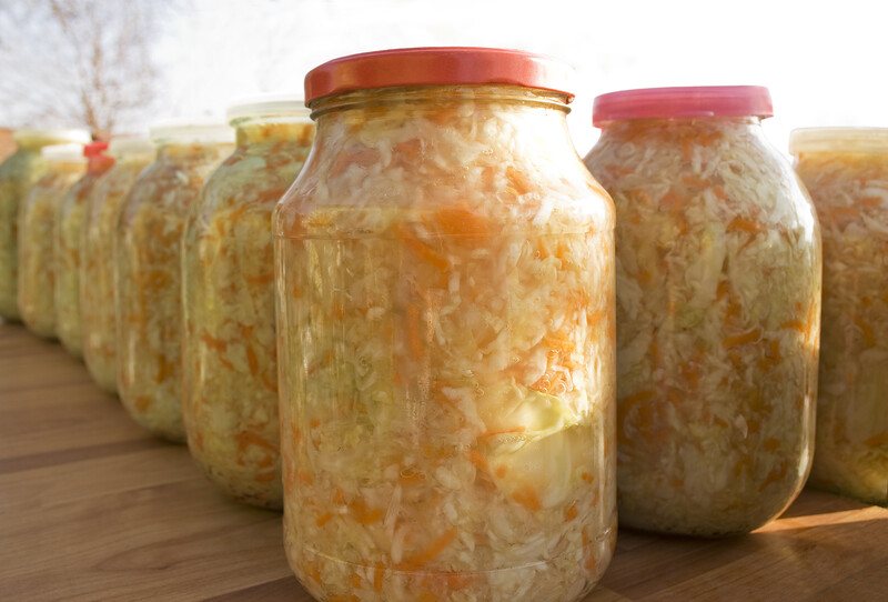 Several jars of sauerkraut rest on a wooden table outside.