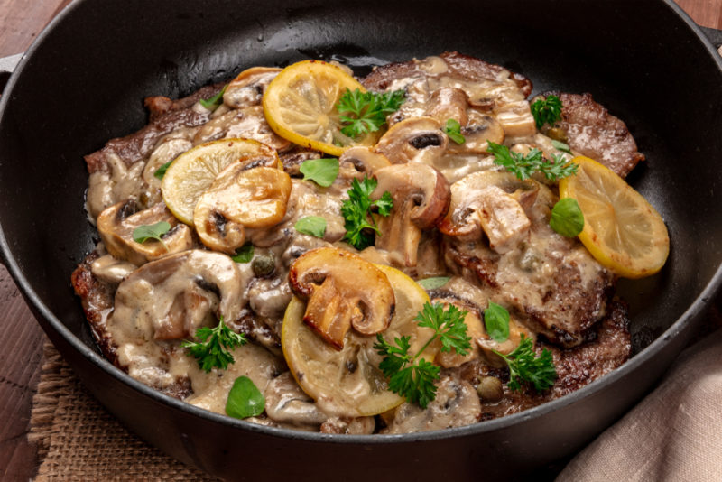 Scallopine di vitello in a black pan, a traditional dish that includes mushroom sauce and lemons