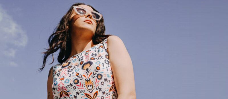 A woman in an interesting dress wearing glasses, standing outside and framed against the sky