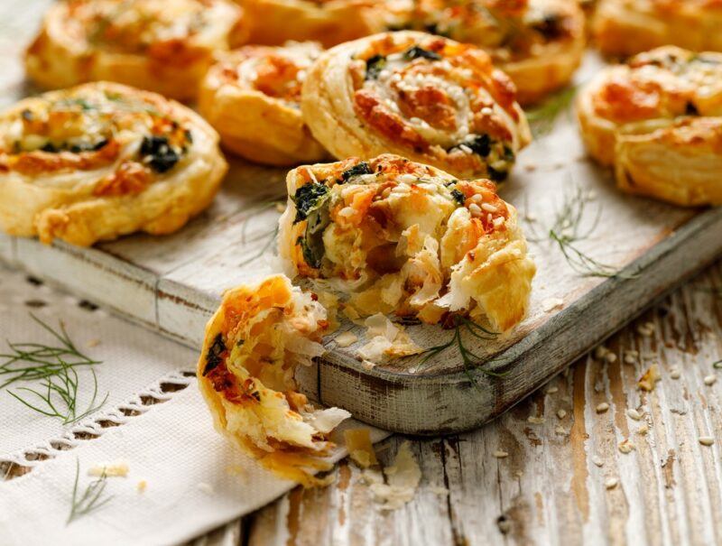 A wooden tray with a close up image of scrolls made using puff pastry, containing spinach and some other ingredients