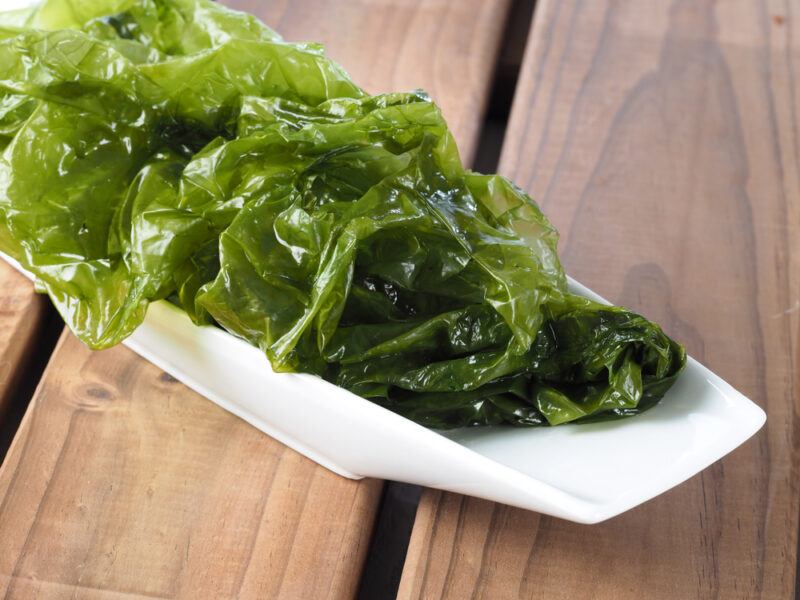 on a wooden surface is a white elongated dish with fresh sea lettuce