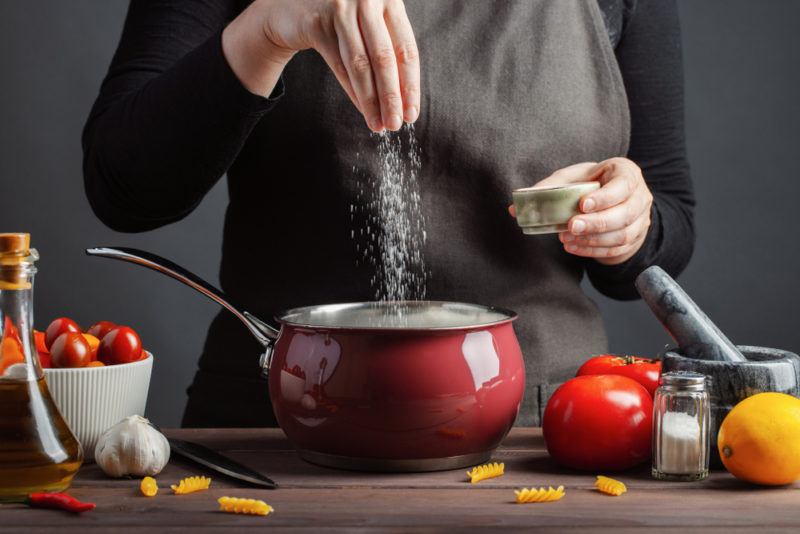 A woman seasoning a meal she's cooking in a red pot