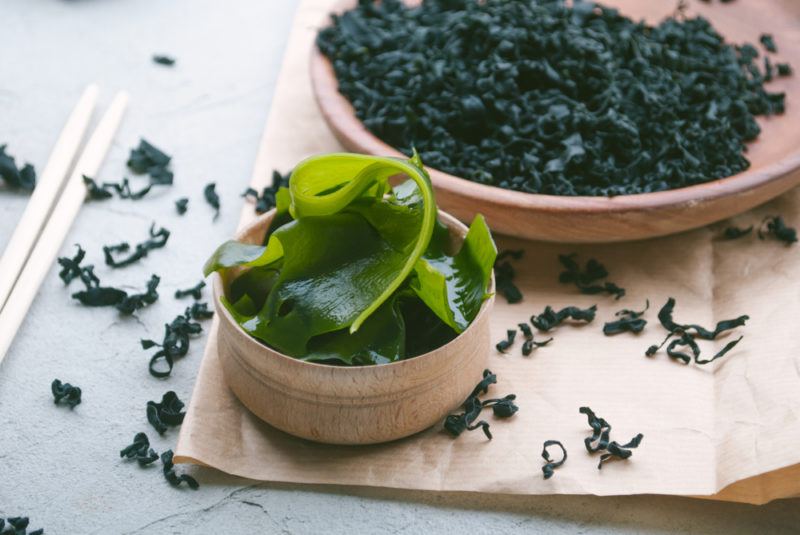 A wooden bowl of dried seaweed and another one of fresh seaweed