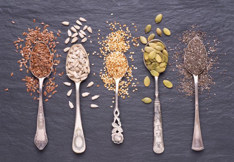 A selection of seeds on spoons on a black background