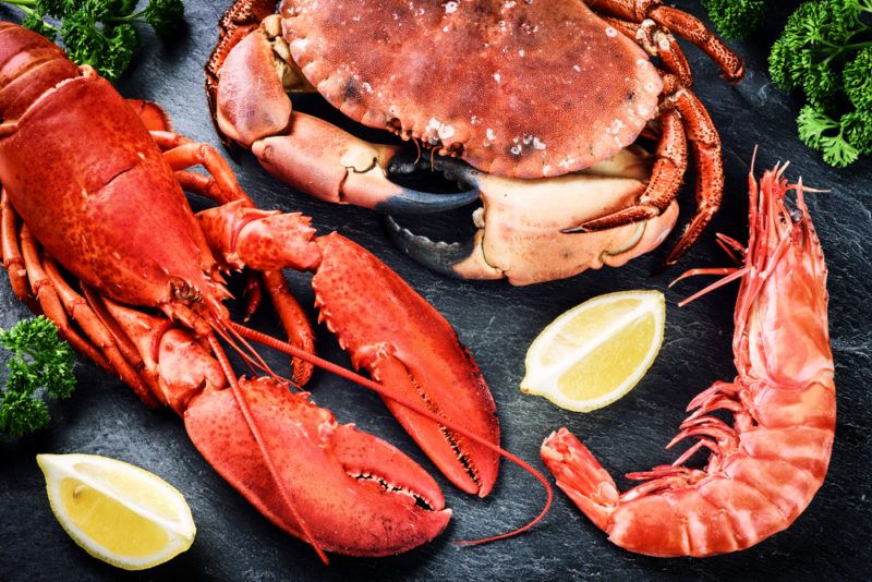 A lobster, a crab and a prawn on a wooden table with lemons