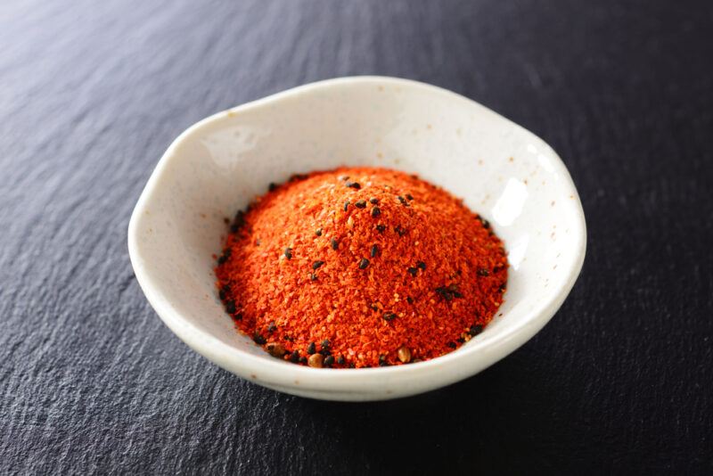 on a black wooden surface is a small white dish with shichimi togarashi seasoning